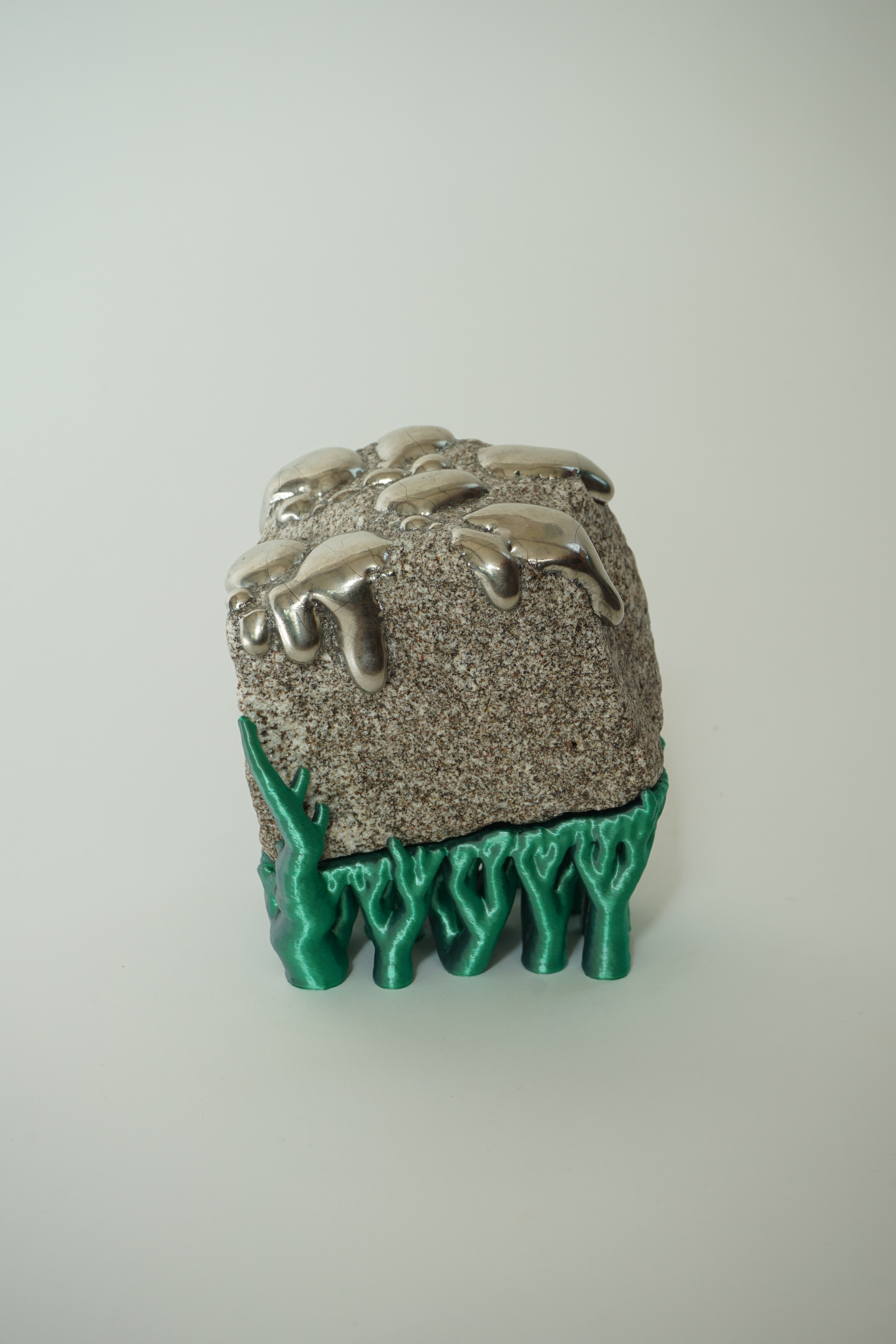 Rooted Silver Drip, sculpture by Sjors Driessen with a natural stone covered in reflective silver lustre droplets and supported by green hyphae-like structures.