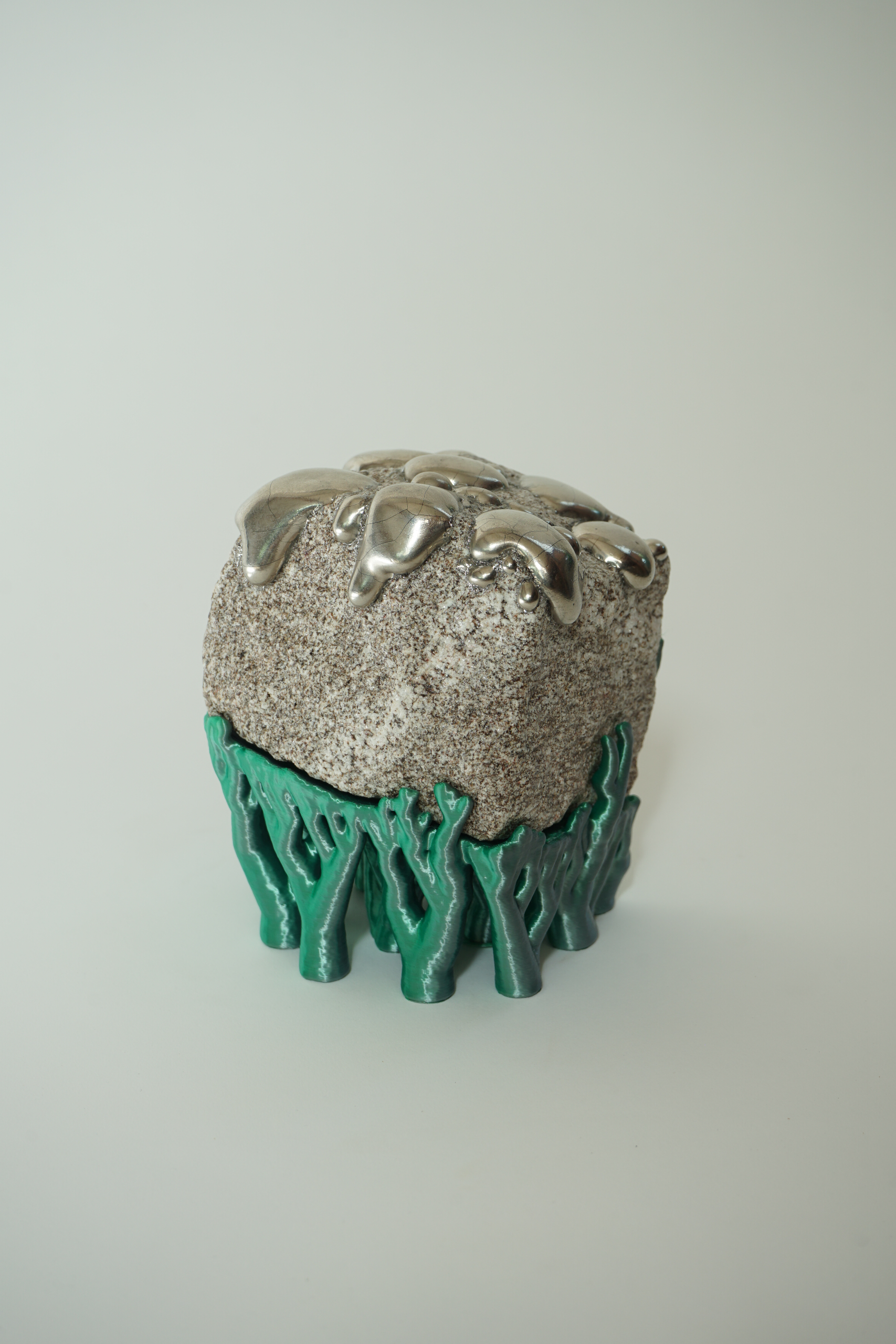 Rooted Silver Drip, sculpture by Sjors Driessen with a natural stone covered in reflective silver lustre droplets and supported by green hyphae-like structures.