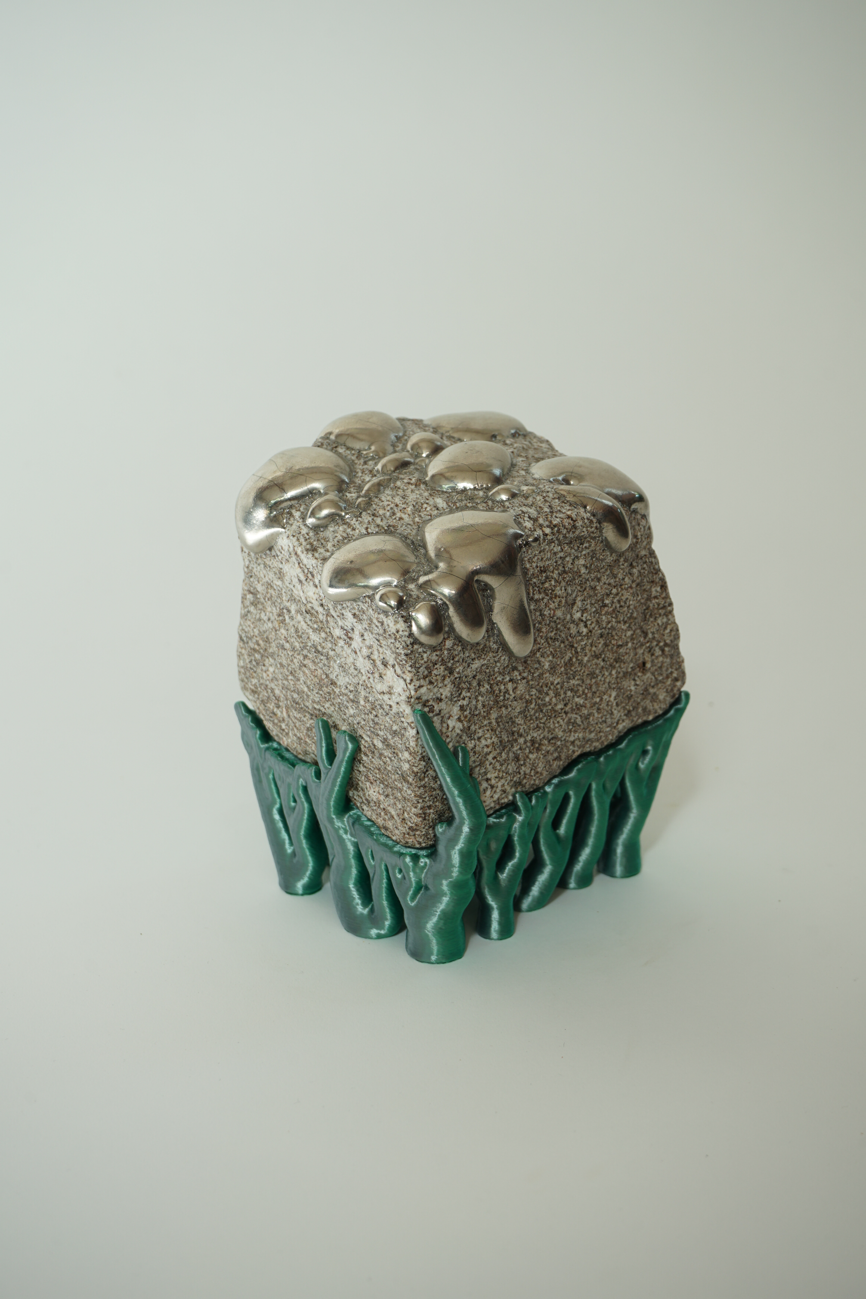 Rooted Silver Drip, sculpture by Sjors Driessen with a natural stone covered in reflective silver lustre droplets and supported by green hyphae-like structures.