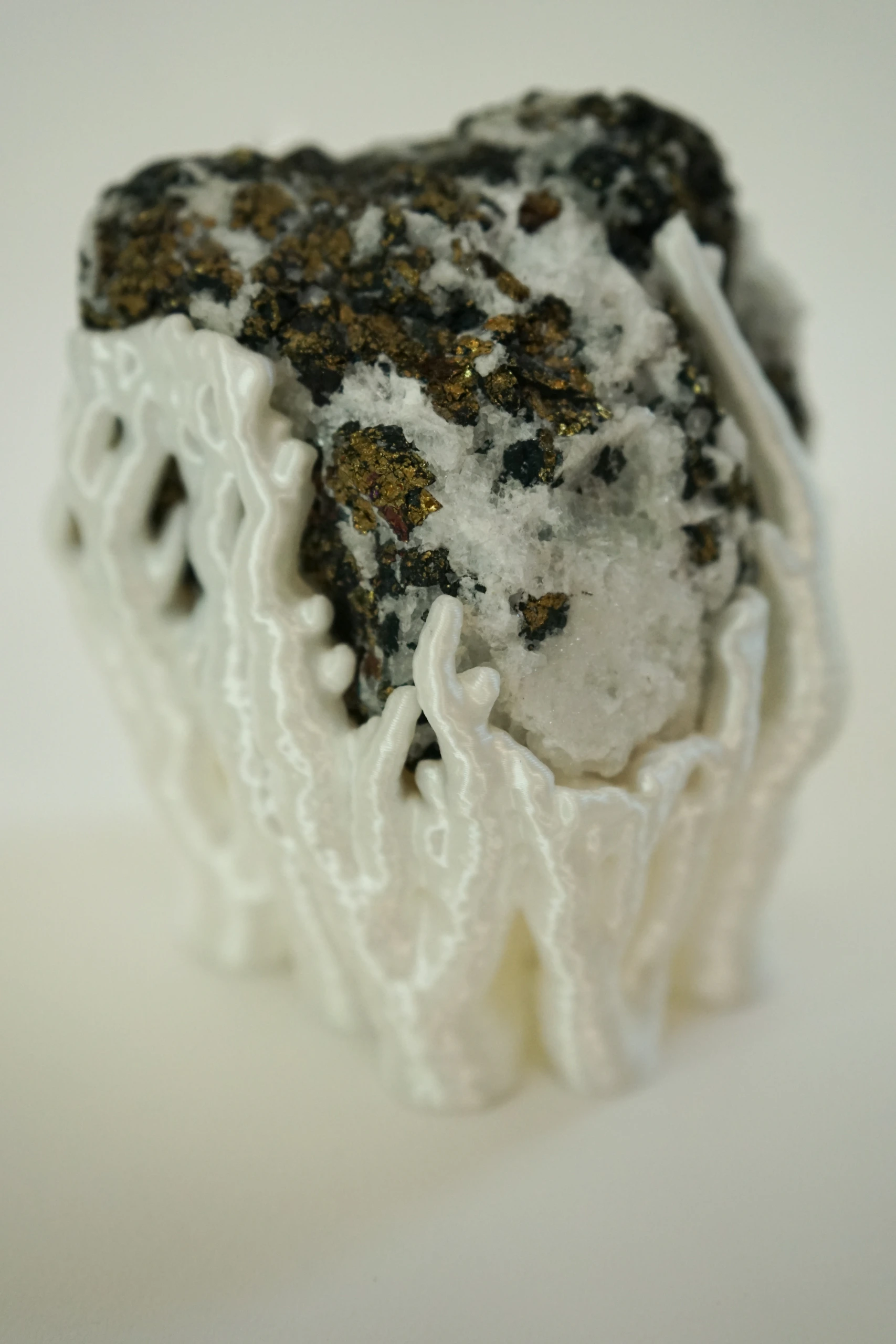 Mineral Cradle, sculpture by Sjors Driessen with a quartz-rich natural stone containing dark and metallic mineral inclusions, held by white branching hyphae-like structures.
