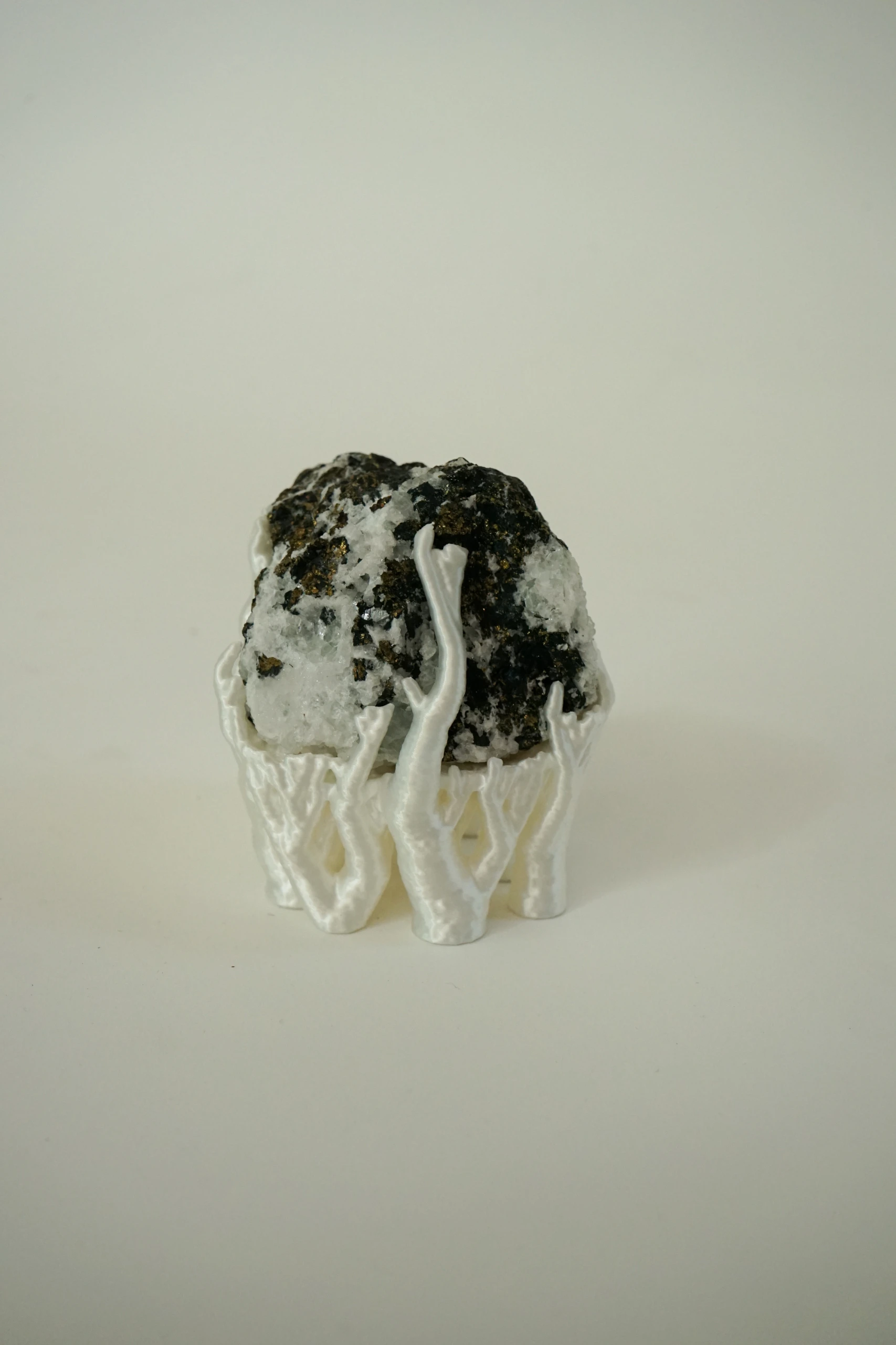 Mineral Cradle, sculpture by Sjors Driessen with a quartz-rich natural stone containing dark and metallic mineral inclusions, held by white branching hyphae-like structures.