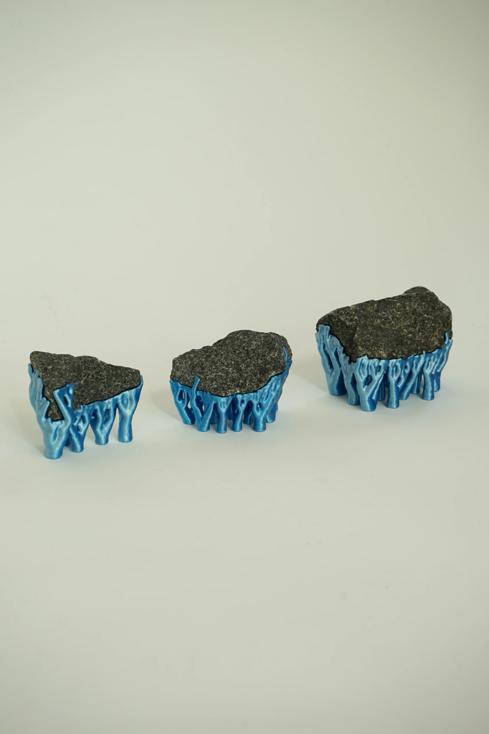 Blue Hyphae III (2026), sculpture by Sjors Driessen with three dark olivine diabase stones supported by bright blue branching hyphae-like structures.