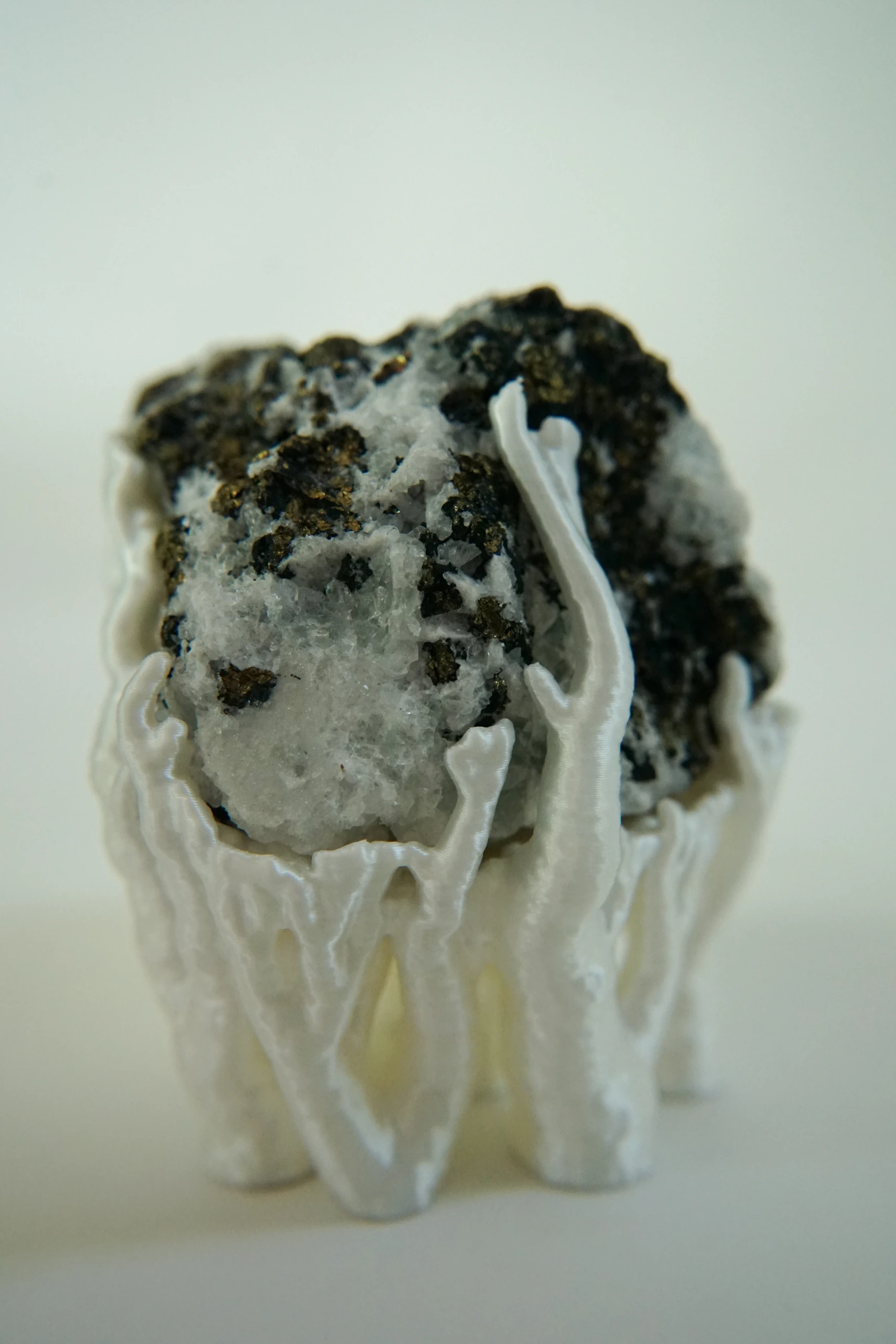 Mineral Cradle, sculpture by Sjors Driessen with a quartz-rich natural stone containing dark and metallic mineral inclusions, held by white branching hyphae-like structures.