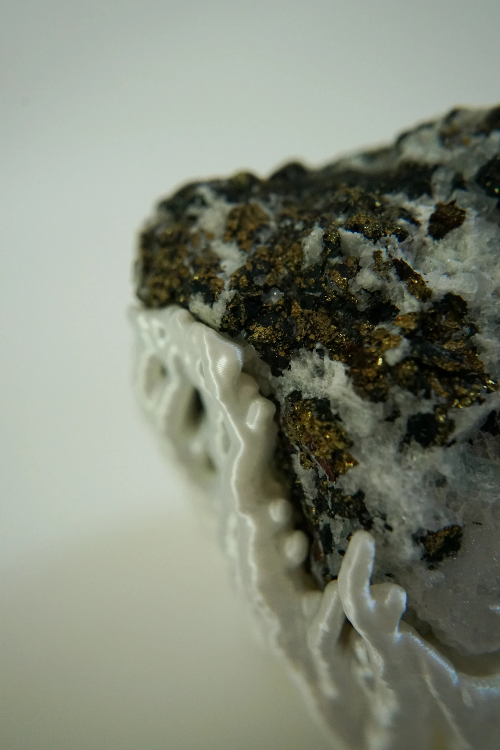 Mineral Cradle, sculpture by Sjors Driessen with a quartz-rich natural stone containing dark and metallic mineral inclusions, held by white branching hyphae-like structures.